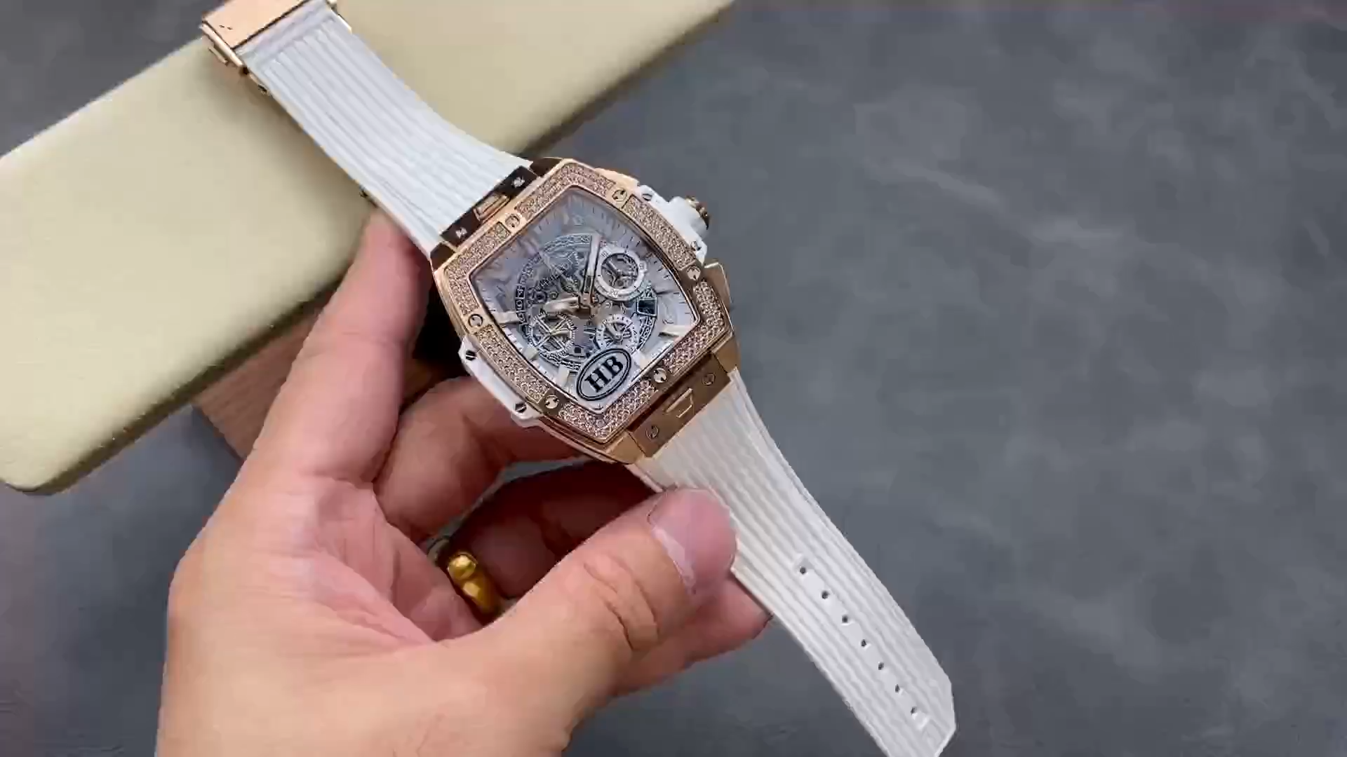 Video of Hublot 642.OE.2010.RW.1204 held in hand, showing the watch and white strap details. - Video