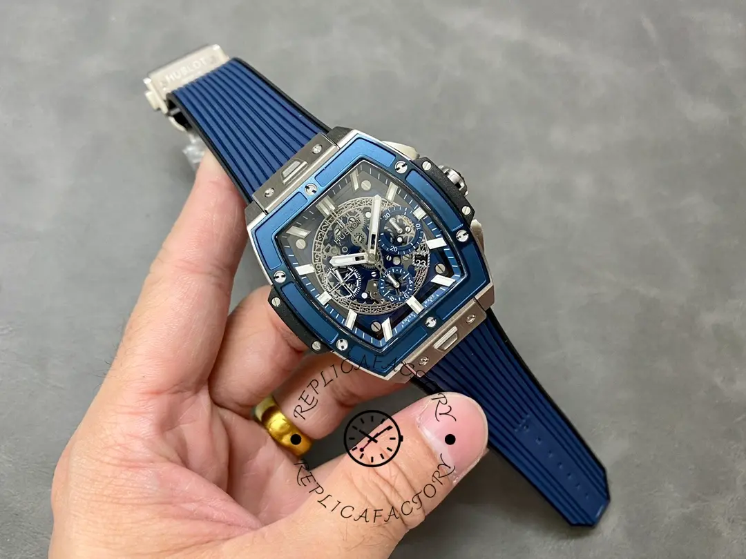 Full watch in hand of Hublot 642.NL.7170.RX showing blue rubber strap and skeleton chronograph layout.