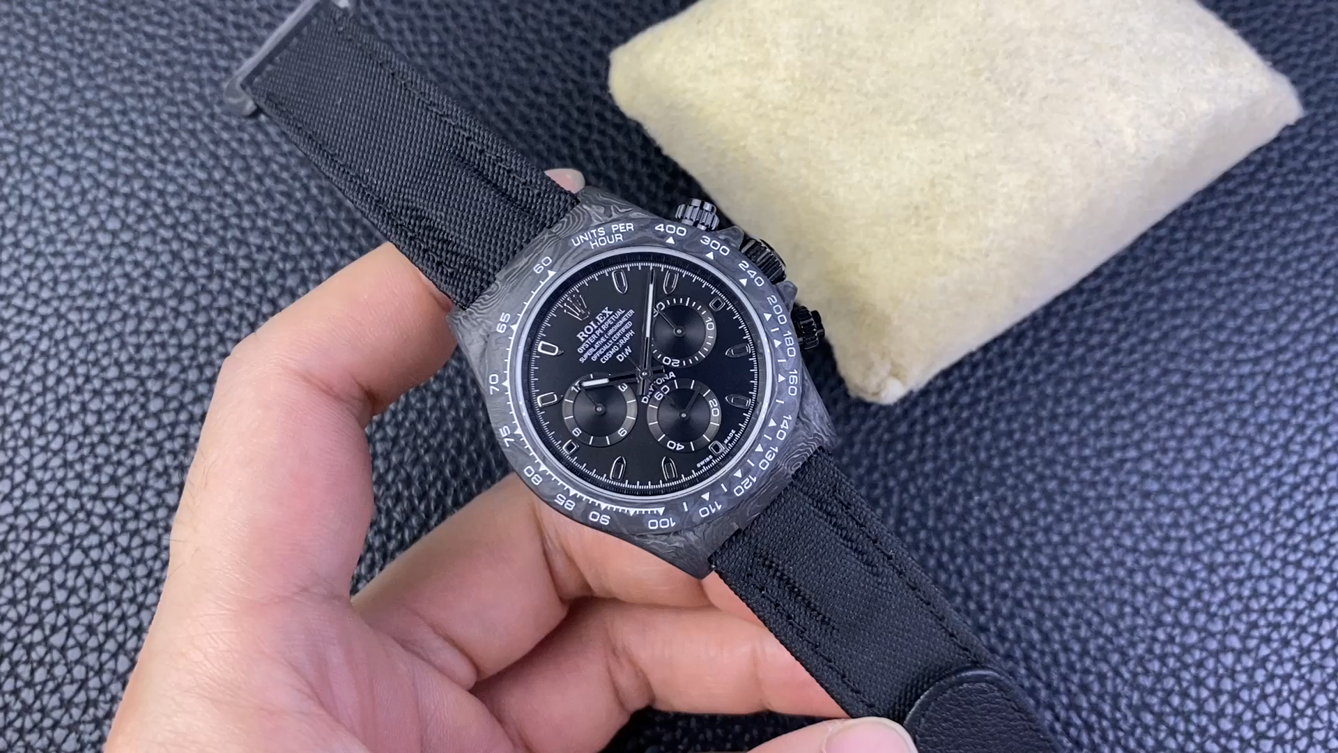 Hand-held view of the Rolex Daytona DIW Black Carbon Case 40mm, showing the black dial and carbon bezel. - Video