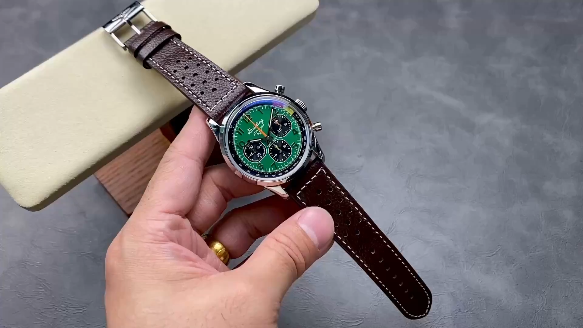 Video: hand-held Breitling Top Time B01 AB01762A1L1X1 showing brown leather strap and case on cushion. - Video