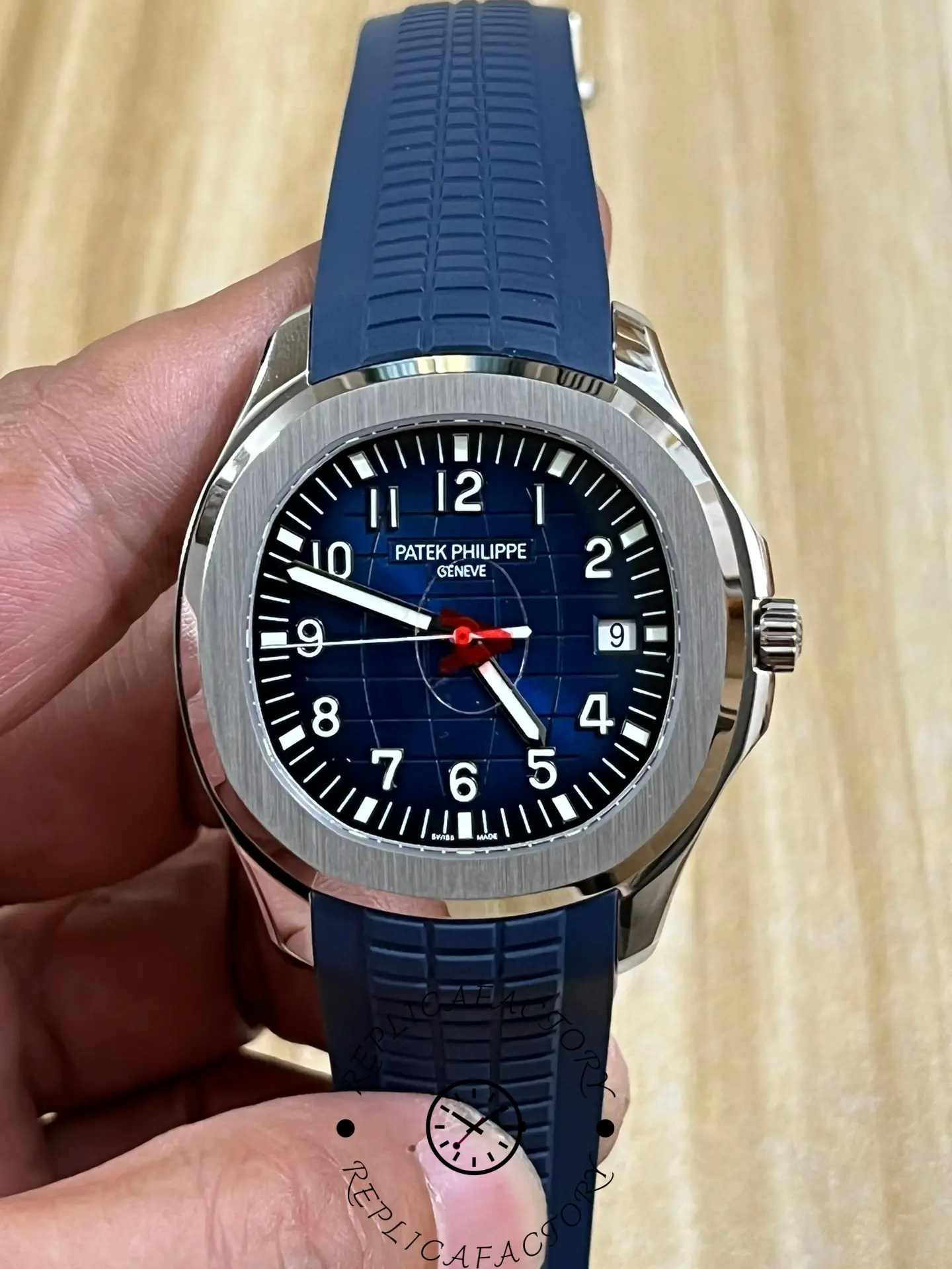 Hand-held front view of Patek Philippe Aquanaut 5168G-001 showing blue dial and red seconds hand.