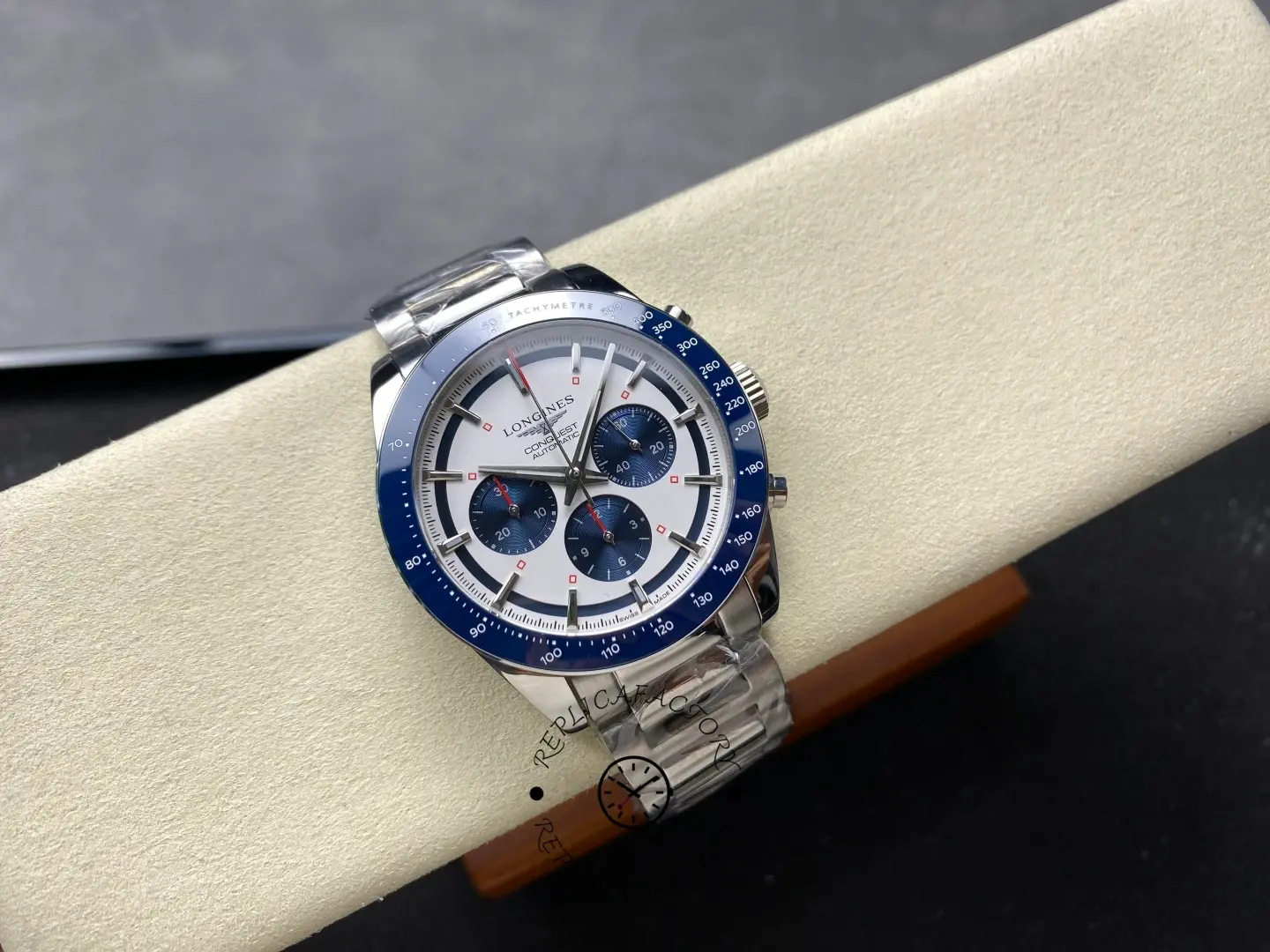 Longines Conquest Chronograph L3.835.4.98.6, full watch on cushion showing blue tachymeter bezel and steel bracelet.