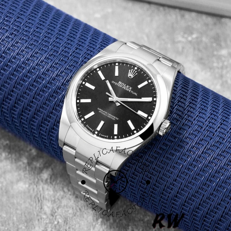 Rolex Oyster Perpetual 114300, black dial, angled shot on blue fabric showing case and bracelet.